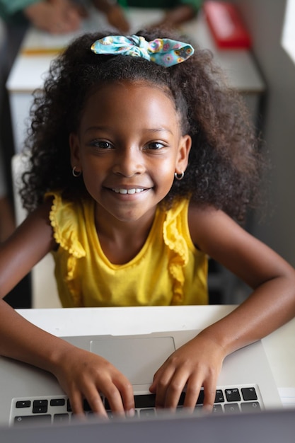 Portret van een glimlachend Afro-Amerikaans basisschoolmeisje met een laptop aan het bureau in de computerklas