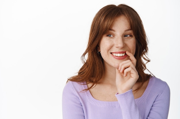 Portret van een glimlachend attent meisje, modieuze kleding en make-up, die er gelukkig uitziet opzij staand op wit