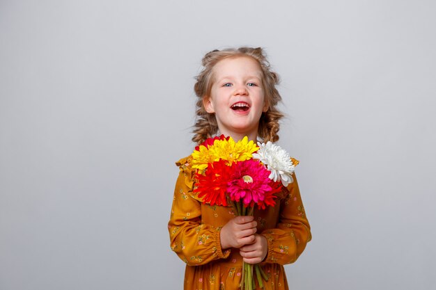 Portret van een glimlachend kind een geïsoleerd blondemeisje met een boeket van bloemen