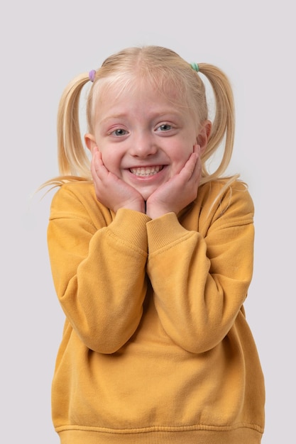 Portret van een glimlachend klein meisje in een gele trui op een witte achtergrond