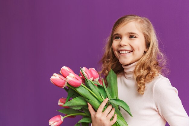Portret van een glimlachend klein meisje met een boeket tulpen geïsoleerd over een violette muur