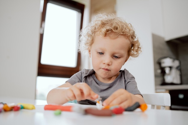 Portret van een glimlachend kleutermeisje dat aan haar keukentafel zit te spelen met plasticine