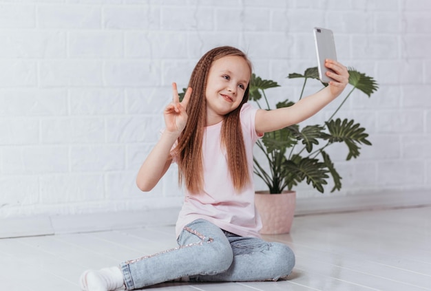 Portret van een glimlachend schattig meisje dat selfie foto maakt op smartphone met overwinning