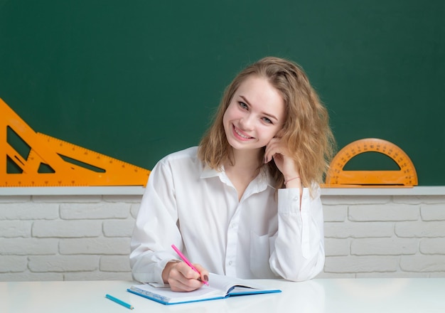 Portret van een glimlachend tienermeisje over schoolbord dat vriendelijk lacht Leuke vrouwelijke studente op de middelbare school