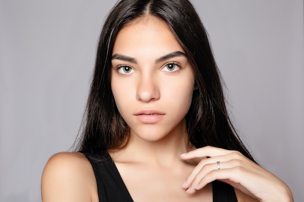 Portret van een glimlachende aantrekkelijke kijken naar de camera. Het dragen van zwarte jurk. Poseren over grijze achtergrond. Mooie lachende vrouw met schone huid, natuurlijke make-up en witte tanden