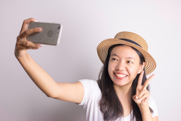 Portret van een glimlachende Aziatische vrouw met hoed die smartphone selfie gebruiken