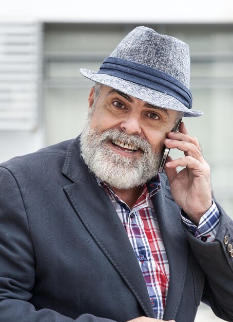 Foto portret van een glimlachende baarde man die een mobiele telefoon beantwoordt in de stad