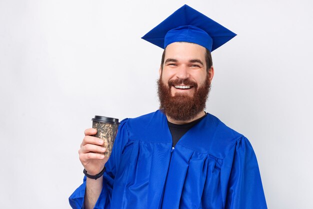 Portret van een glimlachende, bebaarde student die een blauwe vrijgezel draagt en een kopje koffie vasthoudt om mee te nemen