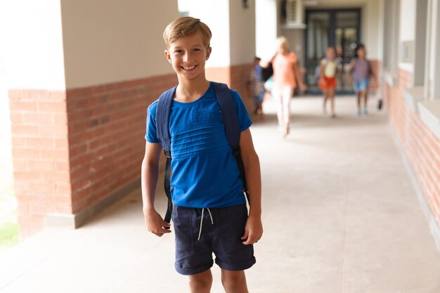 Foto portret van een glimlachende blanke basisschooljongen die in de gang staat