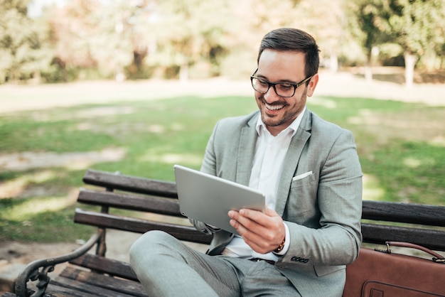 Portret van een glimlachende directeur op een parkbank met digitale tablet.