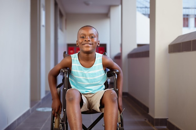 Portret van een glimlachende gehandicapte Afro-Amerikaanse schooljongen die in een rolstoel zit in de gang van de school