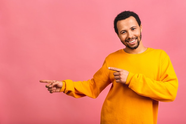 Portret van een glimlachende gelukkige man in casual wijzend met opzij vingers geïsoleerd dan roze.