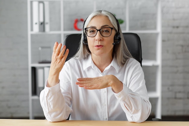 Portret van een glimlachende grijsharige rijpe vrouw die een laptop gebruikt voor een online videogesprek met videoconferenties