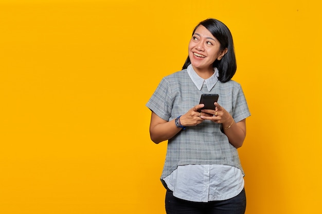 Portret van een glimlachende jonge Aziatische vrouw die een mobiele telefoon vasthoudt en opzij kijkt