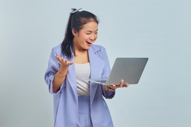 Portret van een glimlachende jonge Aziatische vrouw die naar een laptop kijkt en het succes viert van het krijgen van een nieuw project dat op een witte achtergrond wordt geïsoleerd