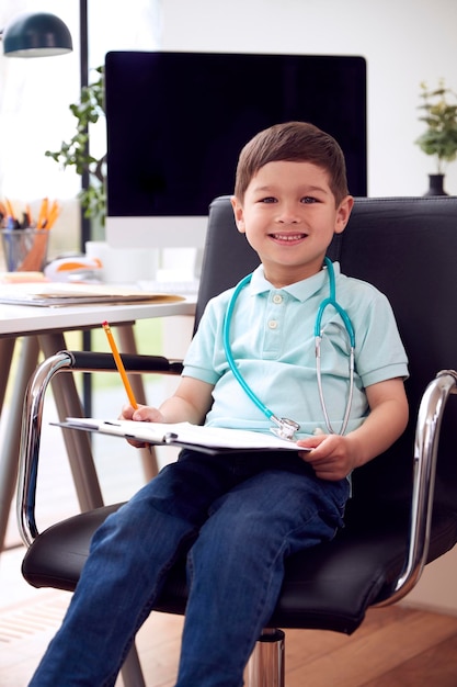 Portret van een glimlachende jonge jongen die in een stoel in het kantoor zit en doet alsof hij dokter is