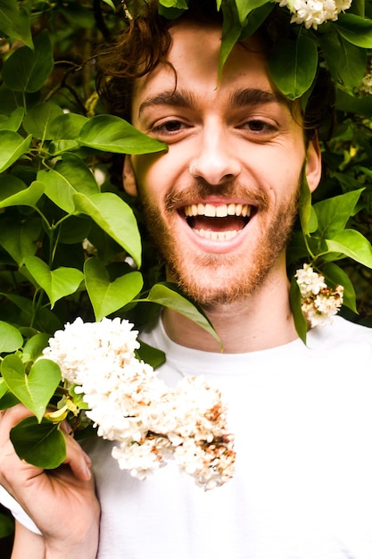 Foto portret van een glimlachende jonge man die bij bloeiende planten staat