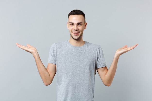 Portret van een glimlachende jonge man in vrijetijdskleding, wijzende handen opzij spreidend