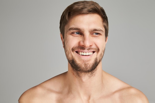 Portret van een glimlachende jonge man met blote zwemmersschouders op een grijze achtergrond krachtige baardcha