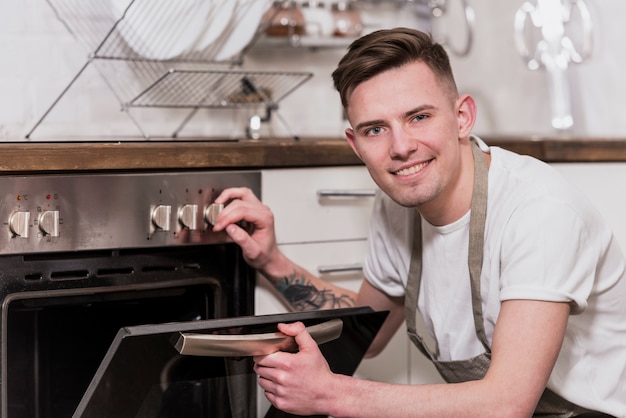 Foto portret van een glimlachende jonge mens die de oven in de keuken opent