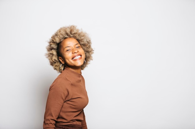 Portret van een glimlachende jonge vrouw die bruine kleren draagt terwijl ze tegen een witte achtergrond staat