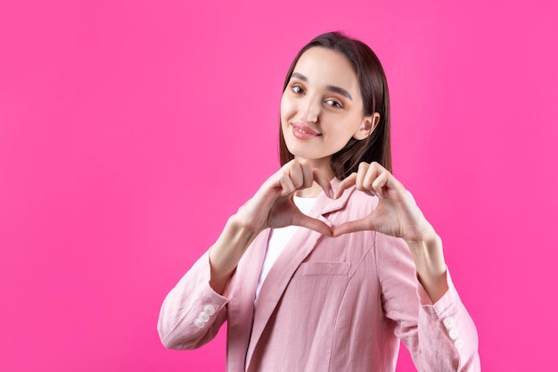 Portret van een glimlachende jonge vrouw die een hartgebaar toont met haar vingers geïsoleerd op pikn-achtergrond