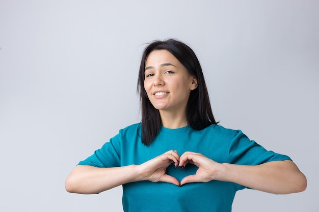 Portret van een glimlachende jonge vrouw die een hartgebaar toont met haar vingers geïsoleerd over grijs