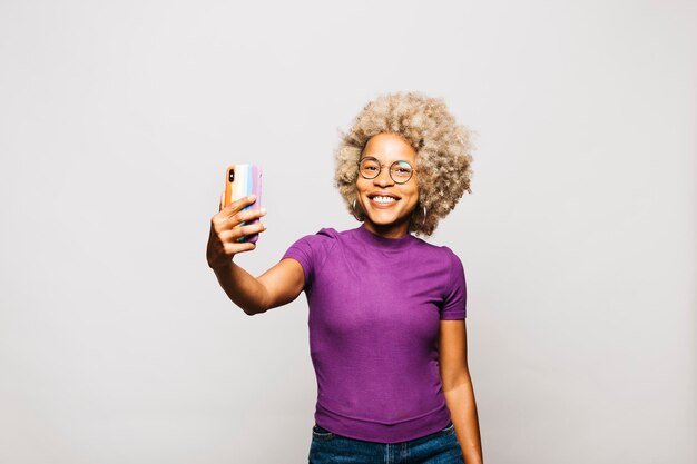 Portret van een glimlachende jonge vrouw die een smartphone gebruikt met een regenboogvlag-hoesje terwijl ze tegen Wh . staat