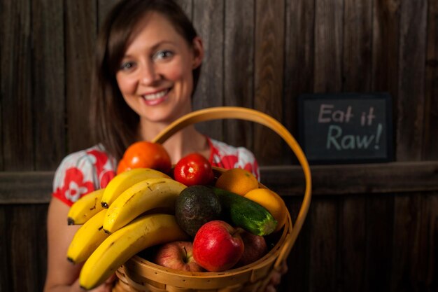 Portret van een glimlachende jonge vrouw die groenten in mand houdt.