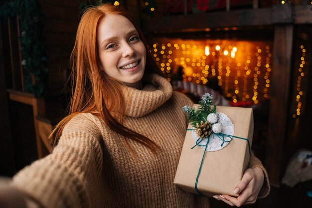 Portret van een glimlachende jonge vrouw die haar vriend bedankt voor een doos met kerstcadeau die naar de camera kijkt