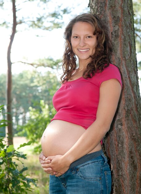 Foto portret van een glimlachende jonge vrouw die op een boomstam staat