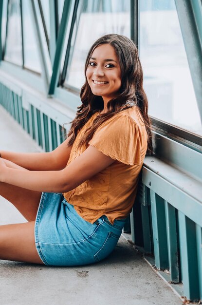 Portret van een glimlachende jonge vrouw die op een voetgangersbrug zit