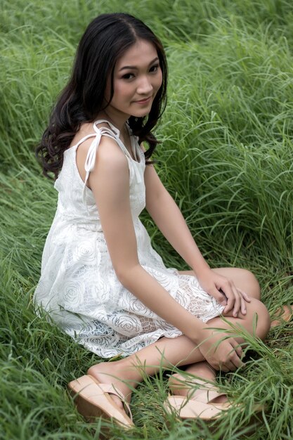 Foto portret van een glimlachende jonge vrouw die op het veld zit