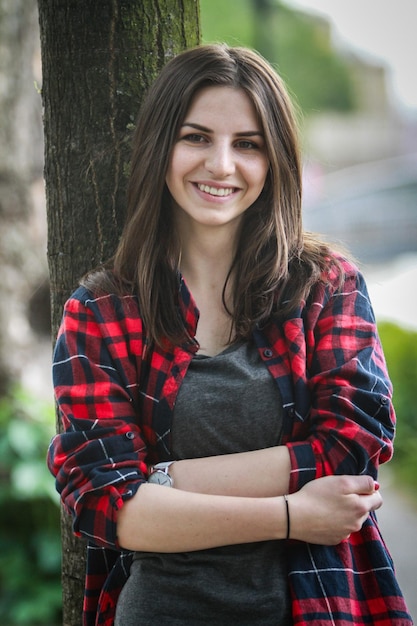 Foto portret van een glimlachende jonge vrouw die tegen een boomstam staat