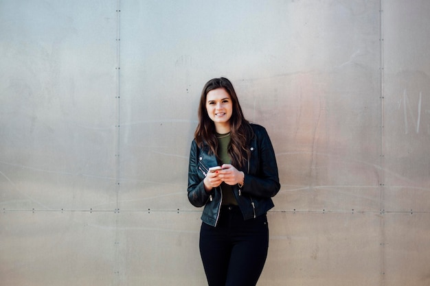 Portret van een glimlachende jonge vrouw die tegen een metalen muur staat