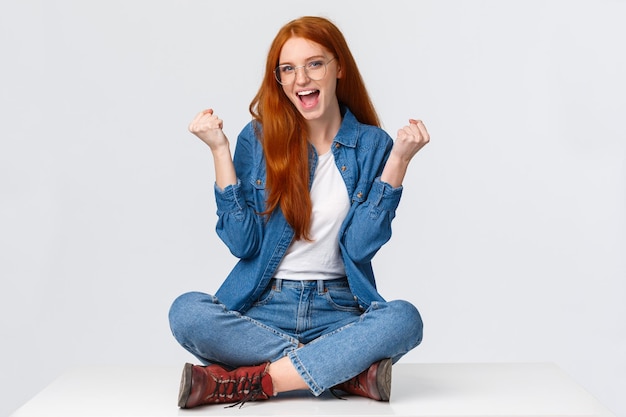 Portret van een glimlachende jonge vrouw die tegen een witte achtergrond zit