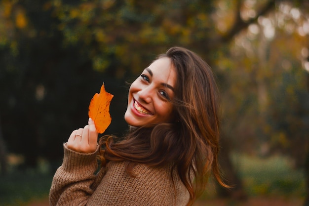 Portret van een glimlachende jonge vrouw met een herfstblad in het park
