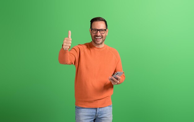 Portret van een glimlachende jonge zakenman met een bord en een mobiele telefoon op een groene achtergrond