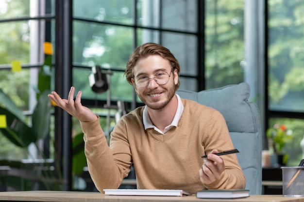 Portret van een glimlachende jongeman die aan het bureau op kantoor voor de camera zit en praat