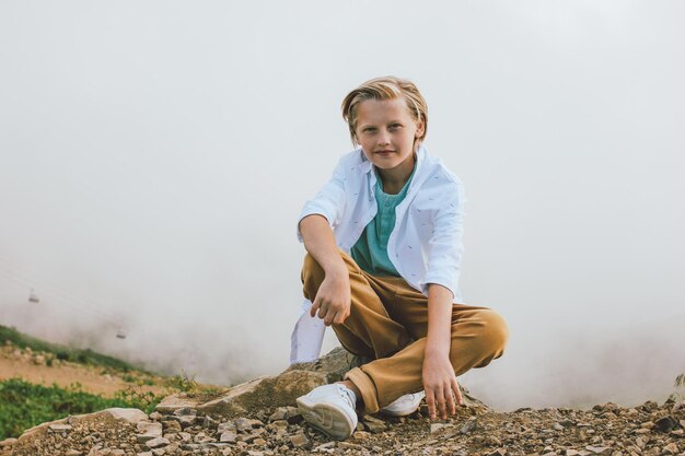 Foto portret van een glimlachende jongen die op een rots tegen de lucht zit