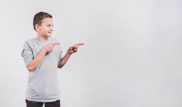 Foto portret van een glimlachende jongen die vingers richt op iets tegen witte achtergrond