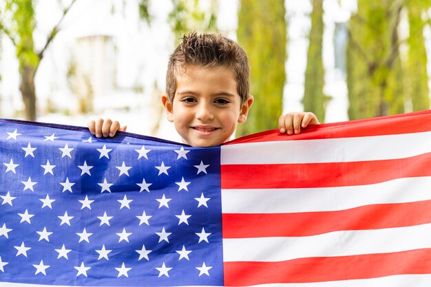 Foto portret van een glimlachende jongen met een amerikaanse vlag in de stad