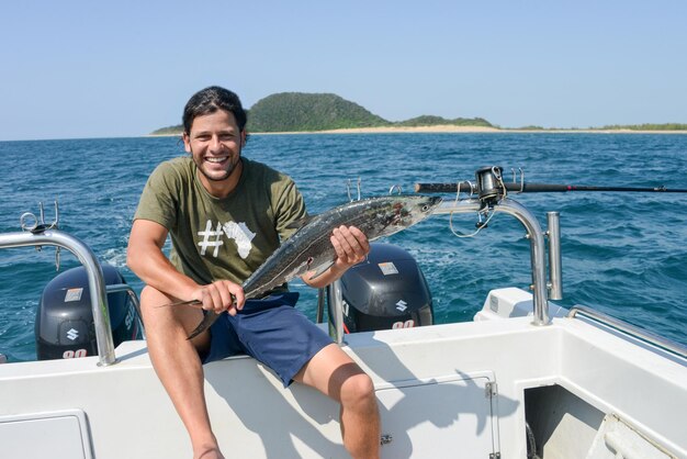 Portret van een glimlachende man die een dode vis vasthoudt terwijl hij op een boot op zee zit