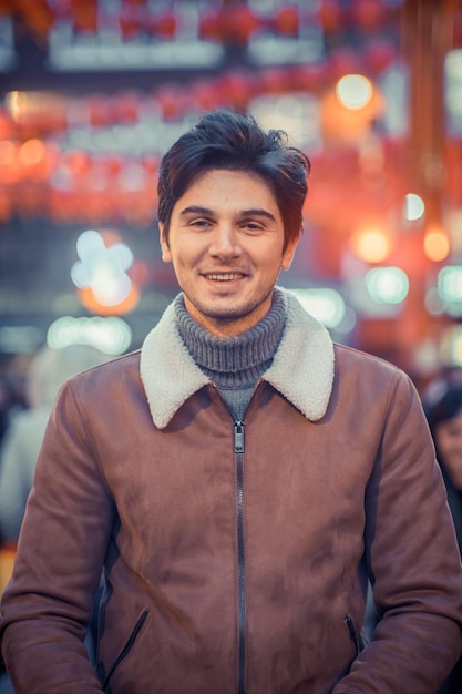 Portret van een glimlachende man die's nachts tegen een verlichte stad staat