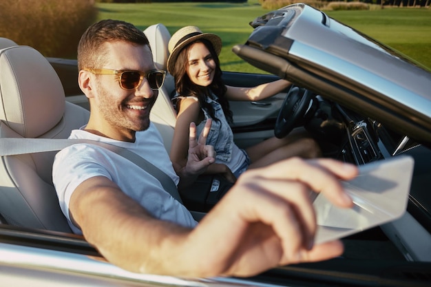 Portret van een glimlachende man die selfie neemt met zijn vriendin op smartphone in de cabriolet