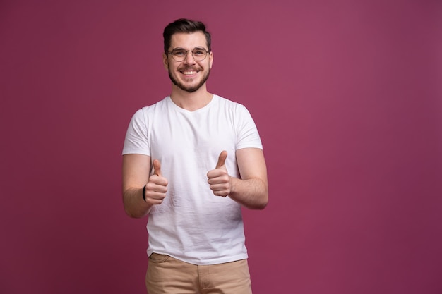 Portret van een glimlachende man in glazen die duim over roze achtergrond tonen.