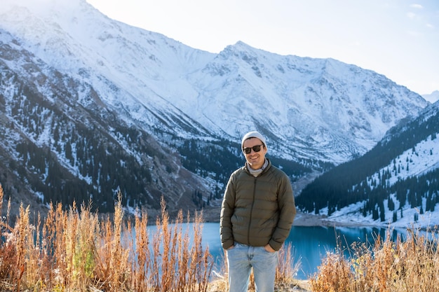 Portret van een glimlachende man in zonnebril over meer omringd door besneeuwde bergen