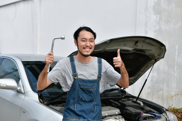 Portret van een glimlachende monteur die tegen de auto staat en gebaren maakt