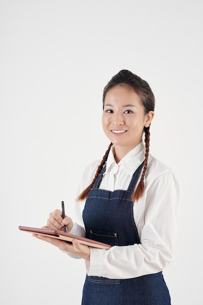 Portret van een glimlachende mooie jonge serveerster die de bestelling accepteert en aantekeningen maakt op de tabletcomputer