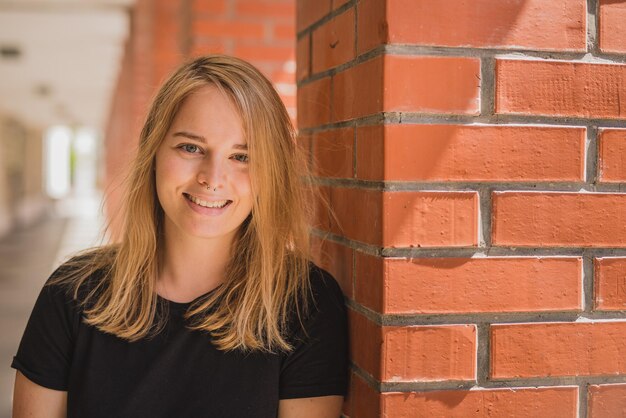 Foto portret van een glimlachende mooie vrouw met blond haar die bij een architectonische kolom staat